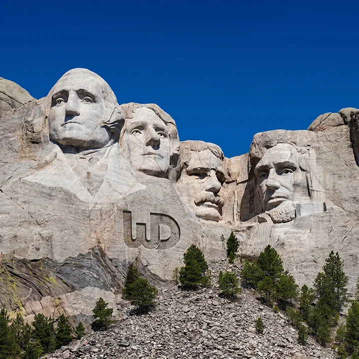 Mount Rushmore monument with a large Womp Designs logo engraved into the rock face below the presidents.