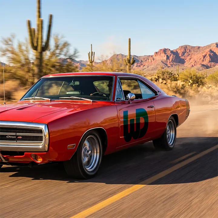 Classic red muscle car with a Womp Designs logo speeding down a desert highway.